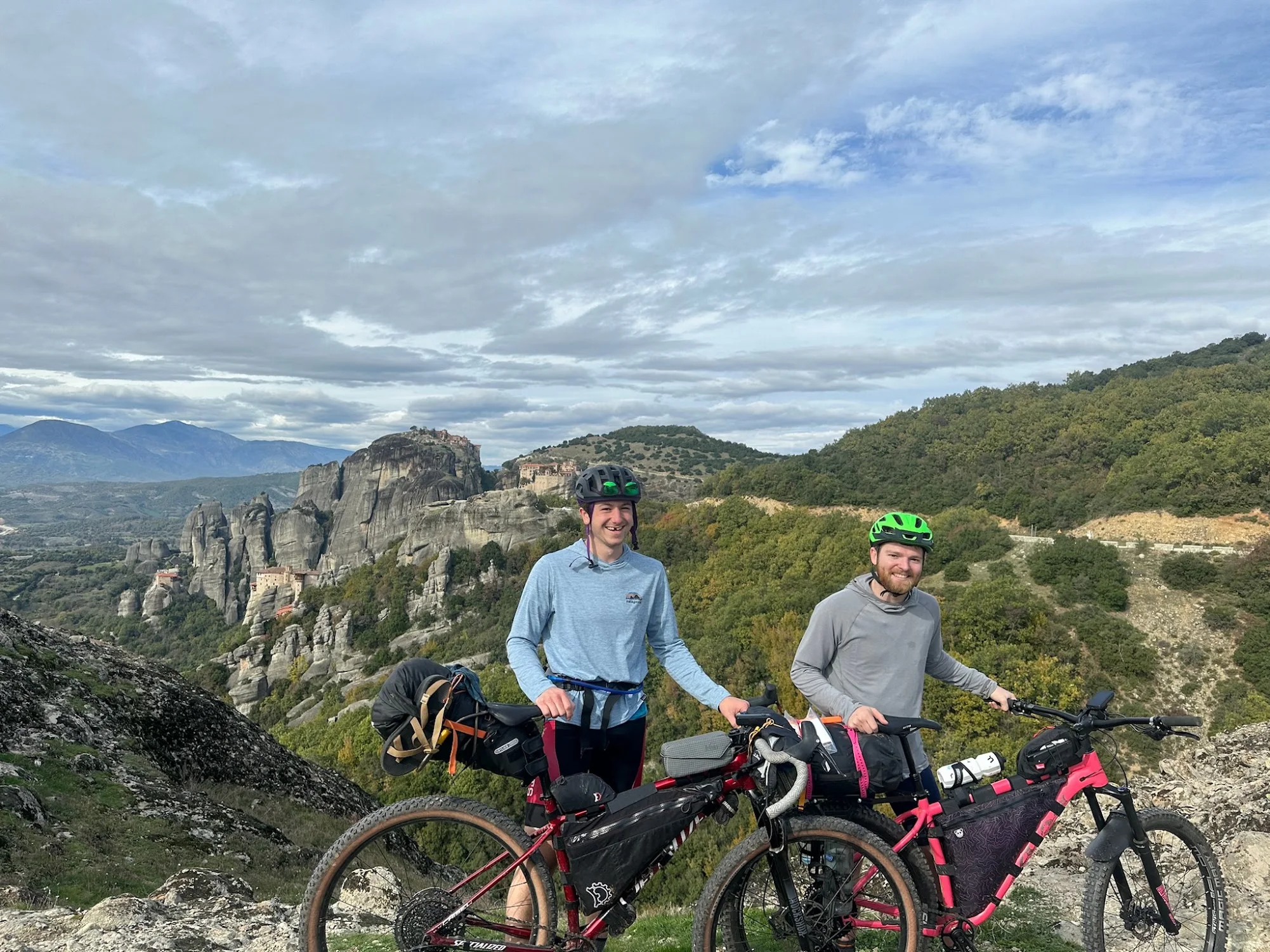 Two cyclists with loaded bicycles at a rocky overlook.
