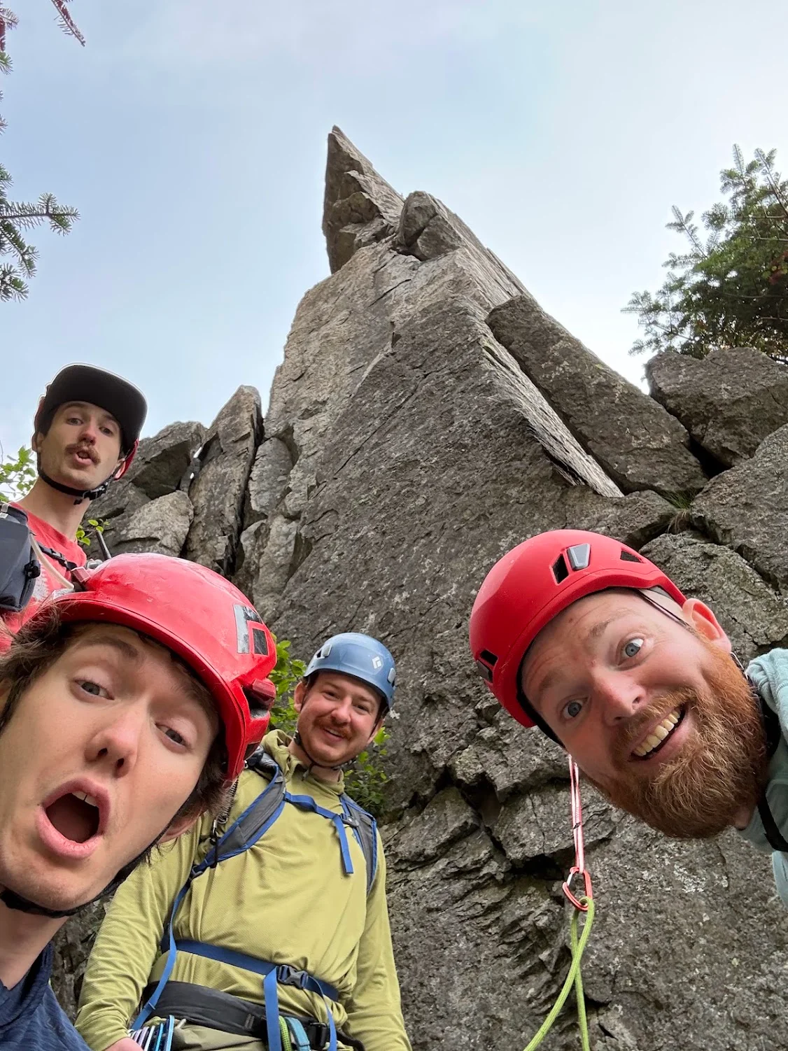 Climbers wearing helmets beside a tall rock formation.