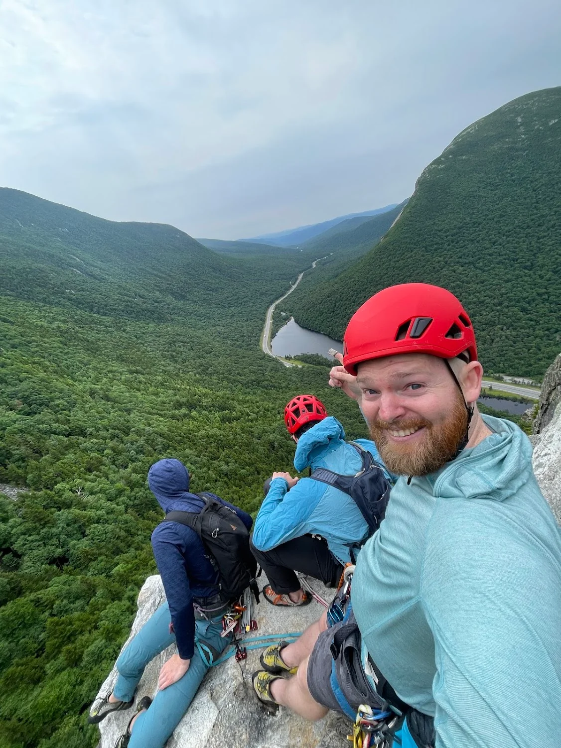 Climbers resting on a ledge above a forested valley.