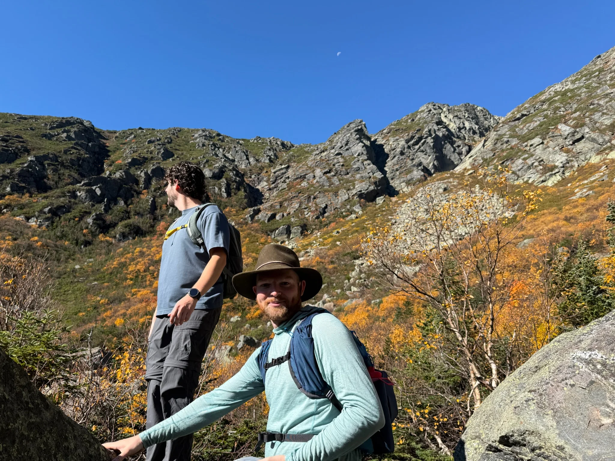 Two hikers on a rocky trail surrounded by autumn foliage.