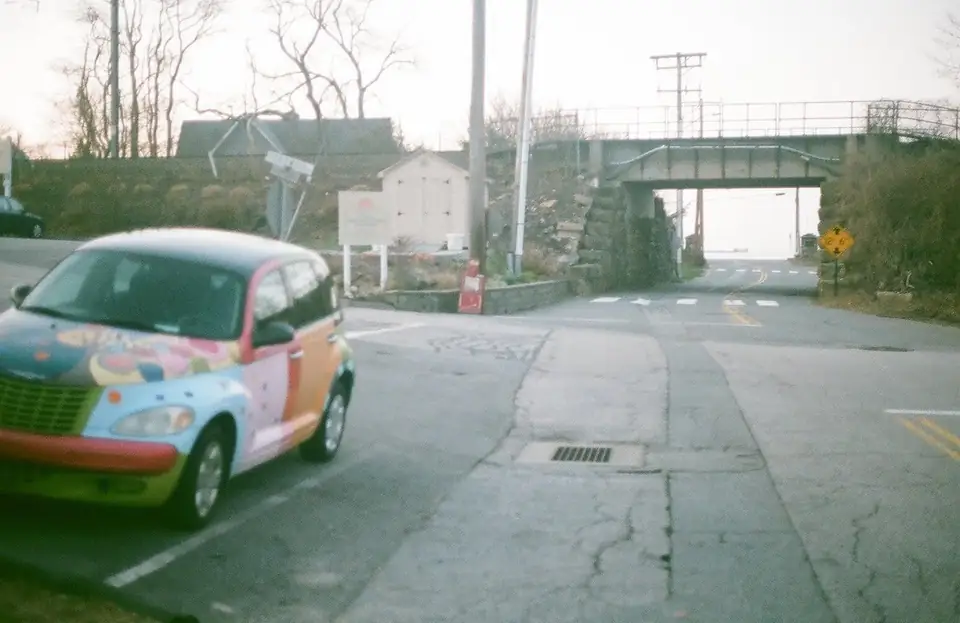 A colorful parked car beside a road and railway bridge.