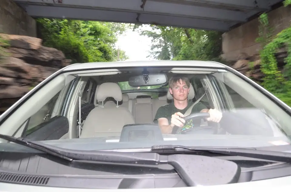 A person in the driver’s seat of a car beneath a bridge.