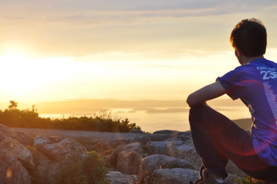 A seated person watching the sunset from rocks.